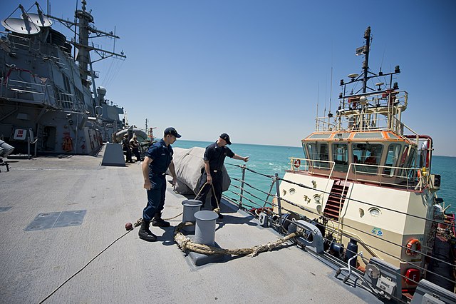 Sailors connect the guided-missile destroyer USS Arleigh Burke (DDG 51) to a tug as the ship prepares to depart Bahrain.
